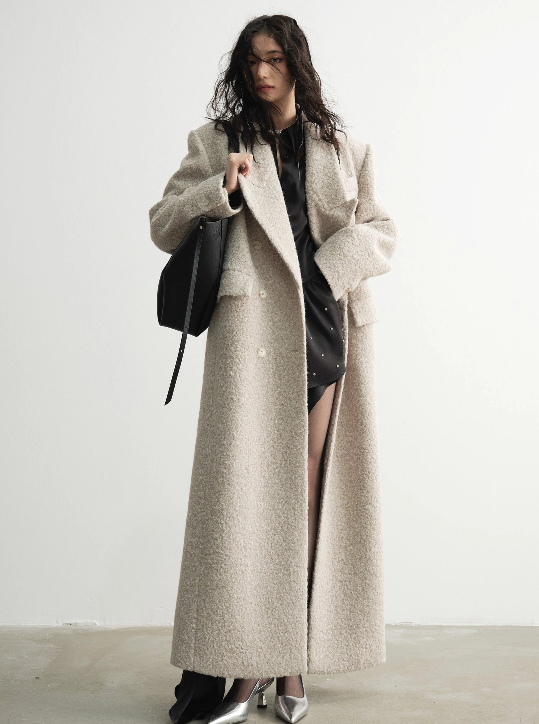 Front three-quarter view of an oversized oatmeal bouclé wool maxi coat with relaxed floor-length silhouette and tailored lapels