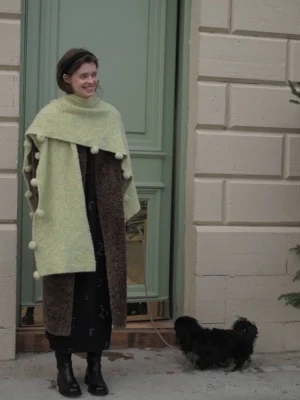 Brown oversized faux shearling long coat with open front styled with a fuzzy scarf in front of a green door