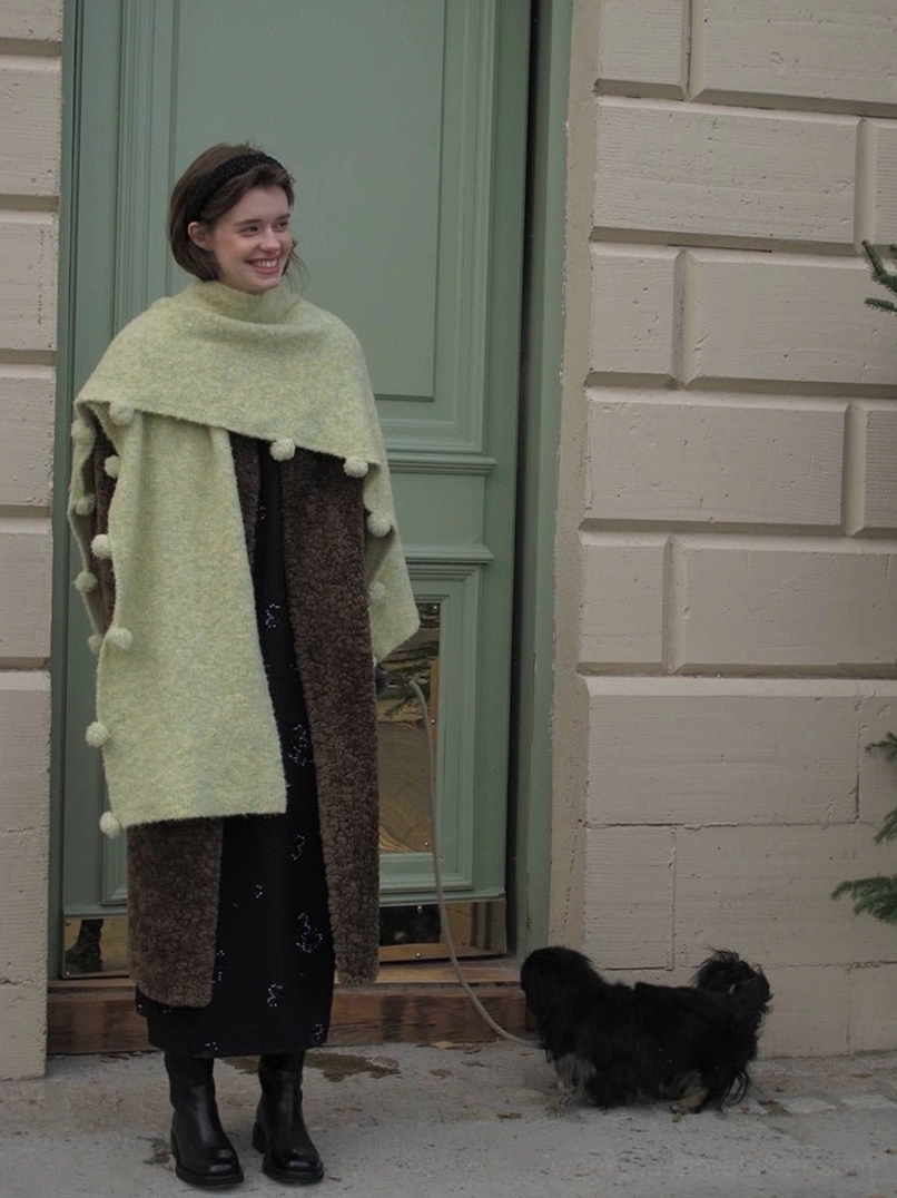 Brown oversized faux shearling long coat with open front styled with a fuzzy scarf in front of a green door