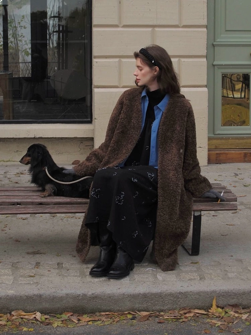 Brown oversized open-front faux shearling long coat for women shown in a side seated street style view