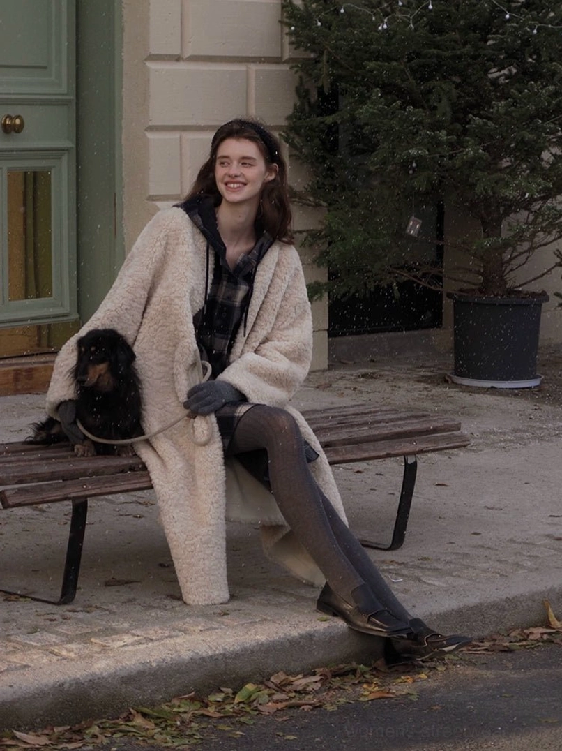 Light cocoa oversized open-front faux shearling long coat for women in a low angle outdoor seated view