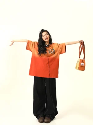 Full body front view of oversized orange ombre Spectra graphic T-shirt styled with black wide-leg pants and crossbody bag