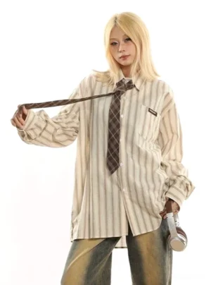Front view of oversized beige striped long sleeve button-up shirt with brown plaid necktie and relaxed dropped shoulders