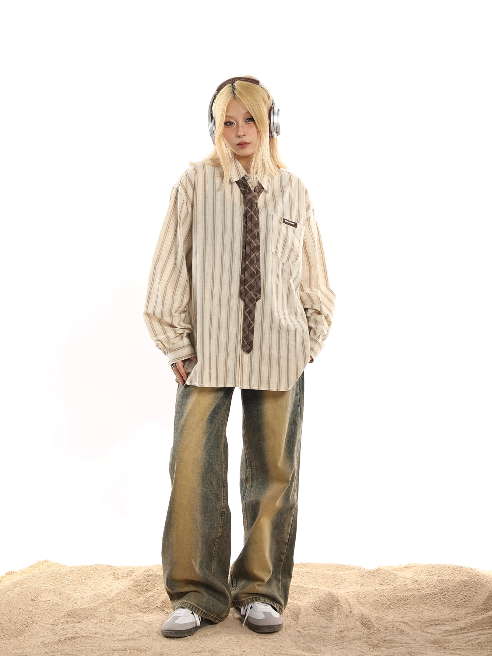 Full body streetwear outfit with oversized pinstripe button-up shirt, brown plaid tie, vintage jeans, and canvas sneakers