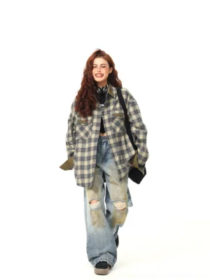 Female model walking in an oversized plaid flannel street shirt layered over black clothing with rolled olive green cuffs and a black crossbody bag