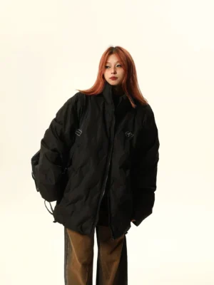Black oversized quilted bomber jacket with stand collar, chest embroidery, hidden pockets, and adjustable drawstring hem styled with brown wide-leg pants