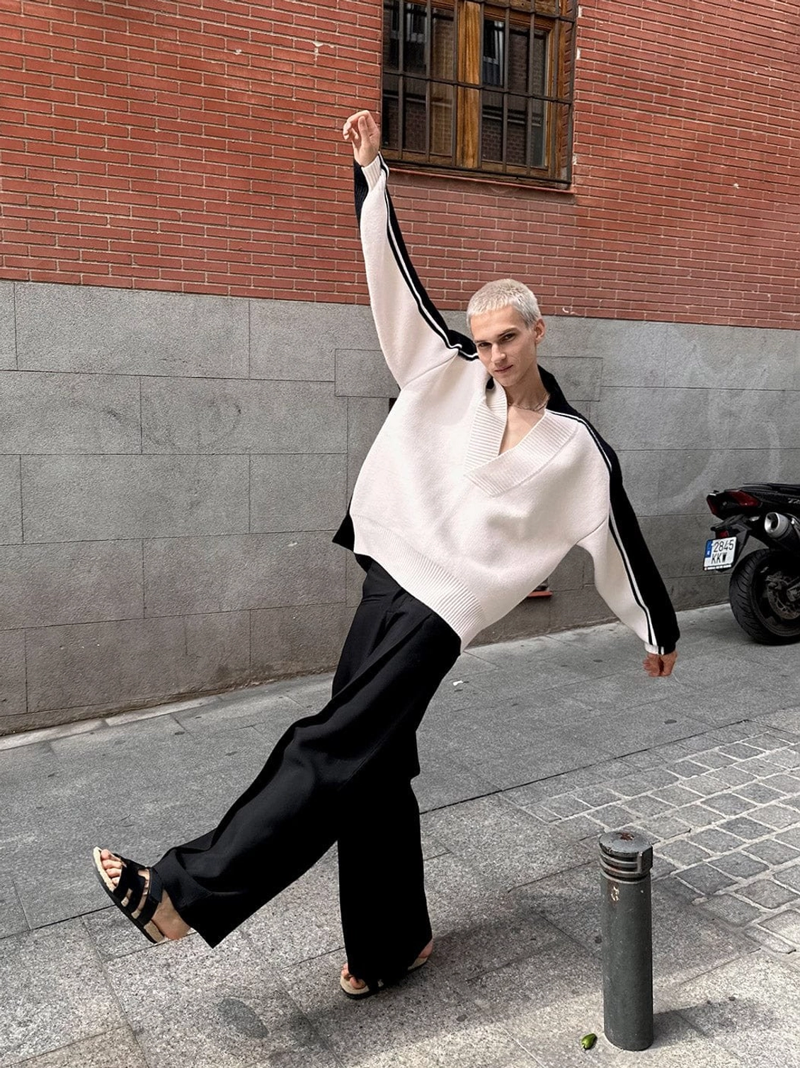 Dynamic full body view of oversized racing stripe sweater styled with wide leg black trousers on an urban street
