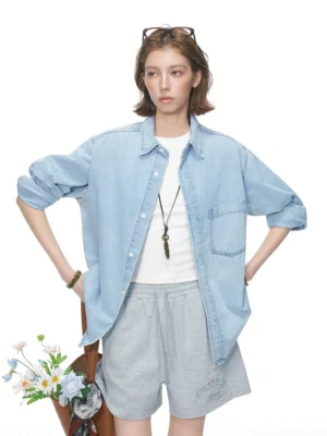 Female model wearing an oversized Retro Blue denim shirt with a relaxed boxy fit, button front, and chest patch pocket in a white studio