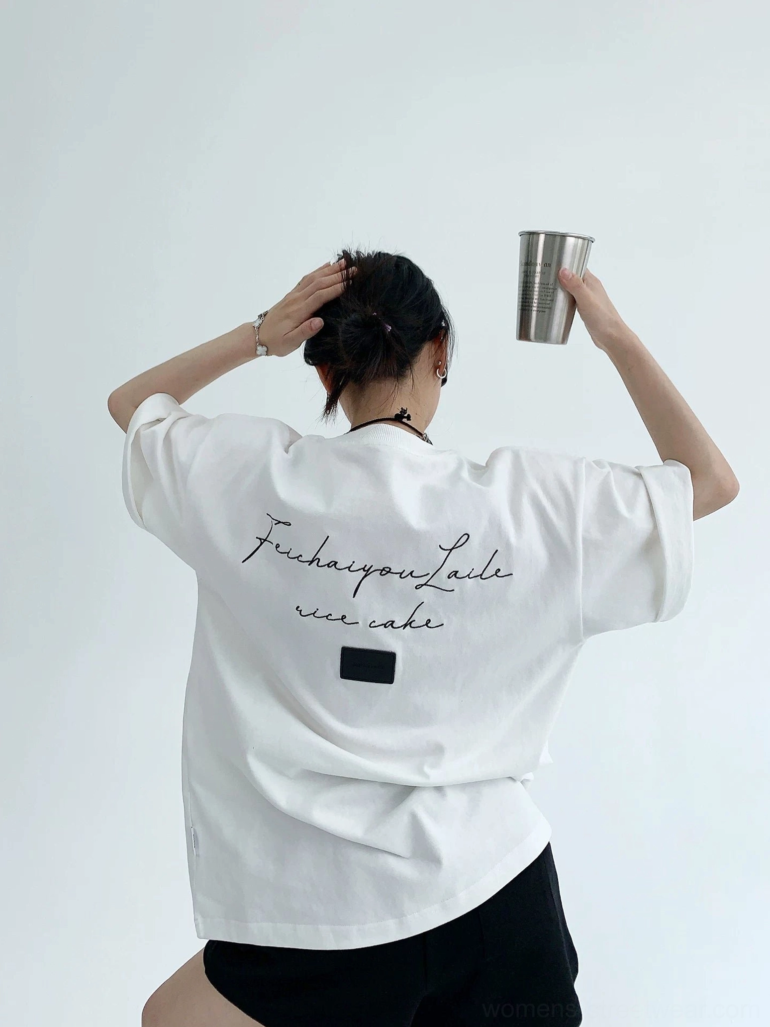 Bright white oversized script back cotton T-shirt with cursive lettering, square fabric patch, rolled sleeves, and casual black shorts