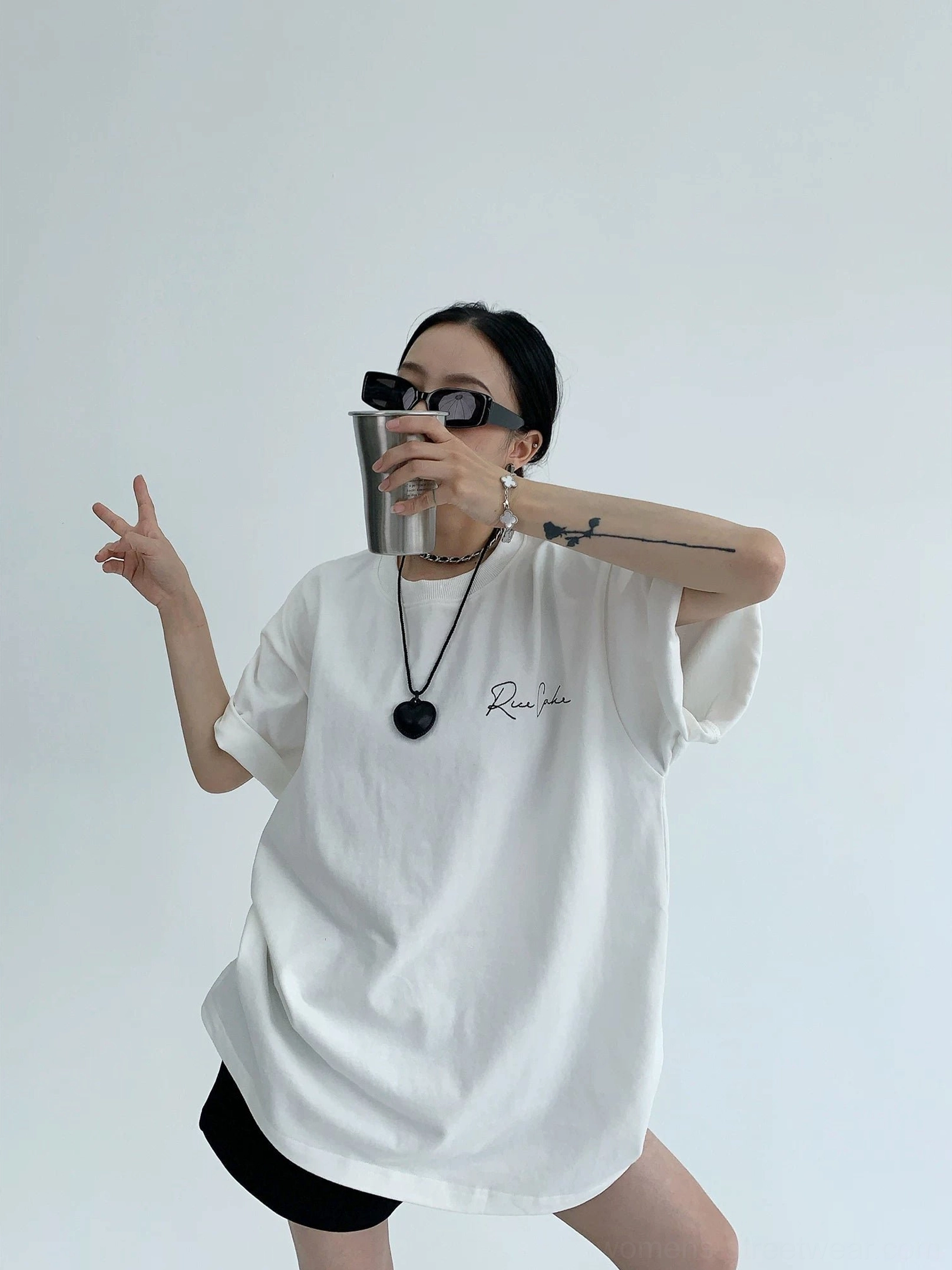 Bright white oversized cotton streetwear T-shirt front view with small cursive chest detail, loose drop shoulders, sunglasses, and pendant necklace