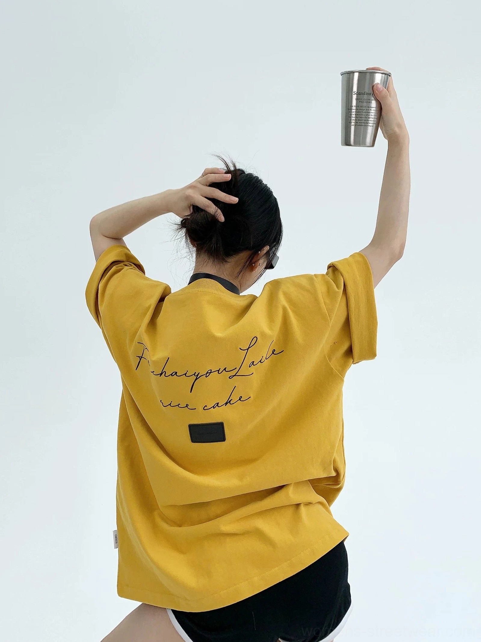 Mustard yellow oversized streetwear T-shirt featuring cursive script lettering, square back patch, relaxed rolled cuffs, and casual styling