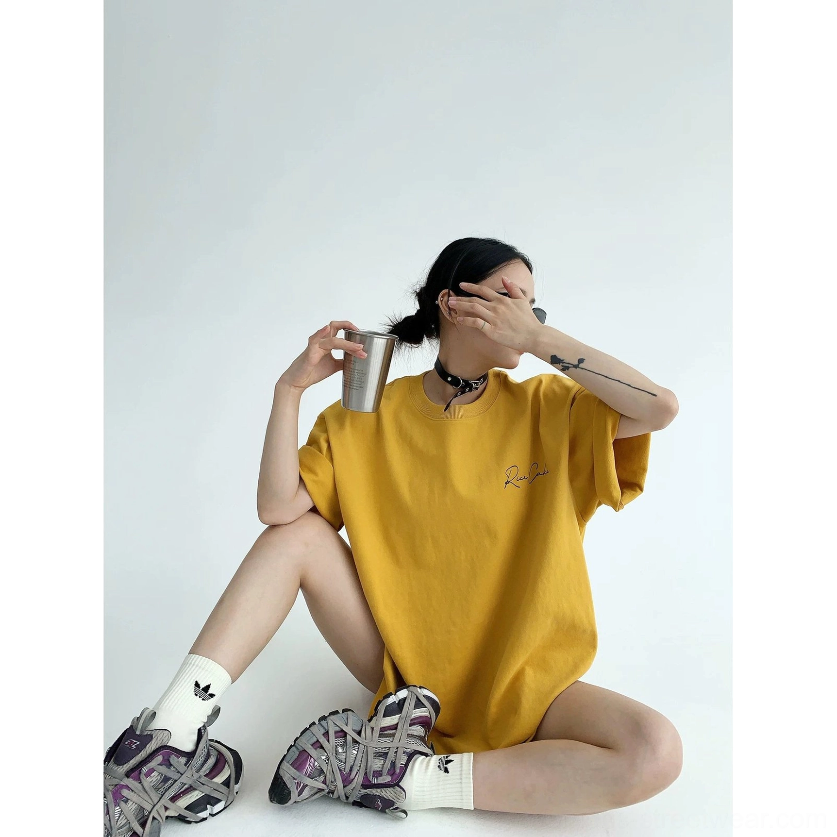 Mustard yellow oversized casual streetwear T-shirt front view with small cursive chest script, loose fit, chunky sneakers, and white socks