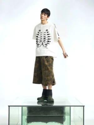 Oversized white skeleton graphic raglan T-shirt styled with camouflage wide-leg pants and dark boots in a streetwear outfit