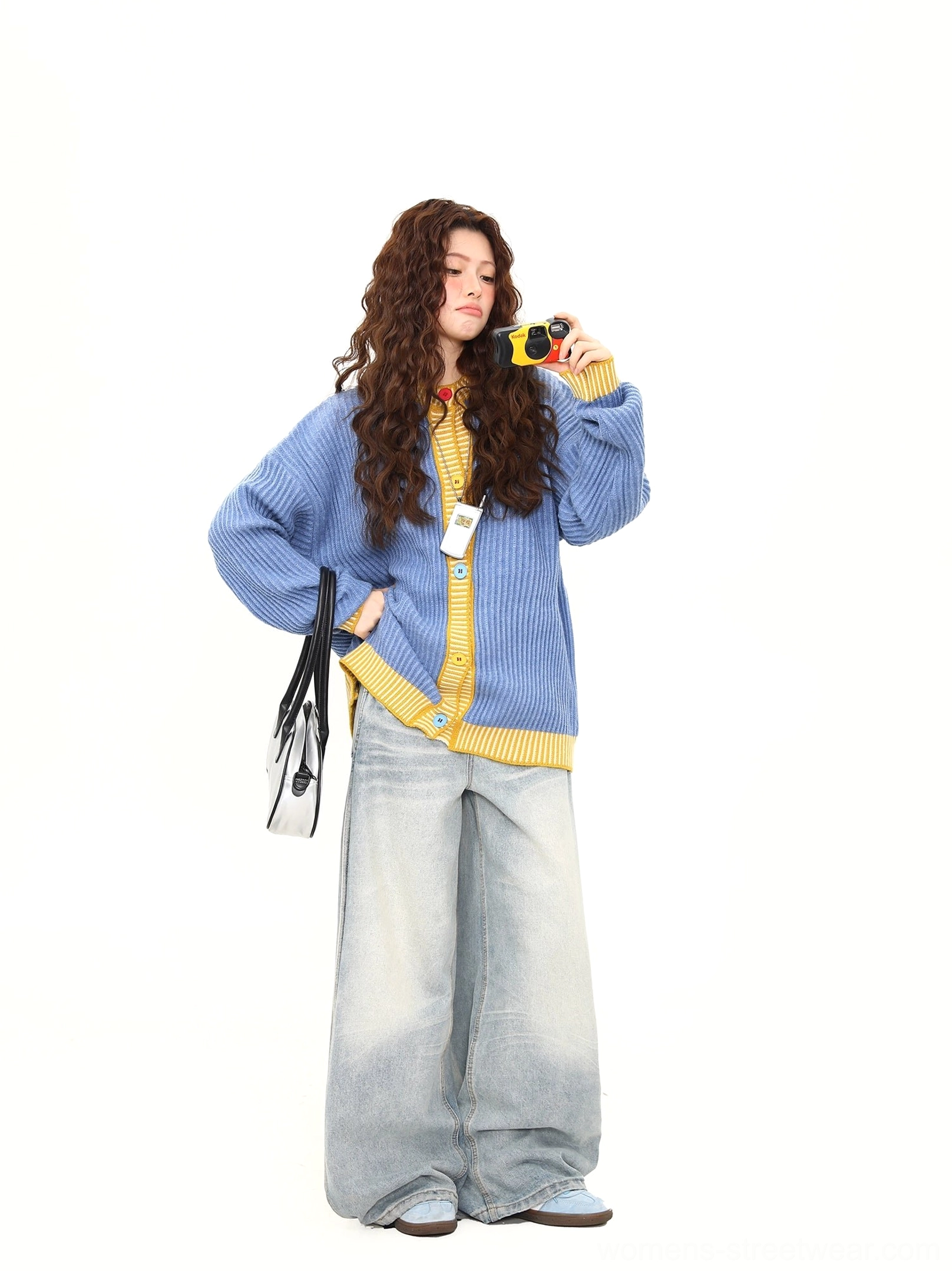 Oversized sky blue ribbed cardigan with yellow striped trims shown from a side three quarter angle with black handbag