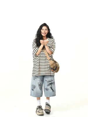 Full-body view of a relaxed oversized striped crew neck T-shirt styled with printed denim shorts, sneakers, white socks, and a canvas bag