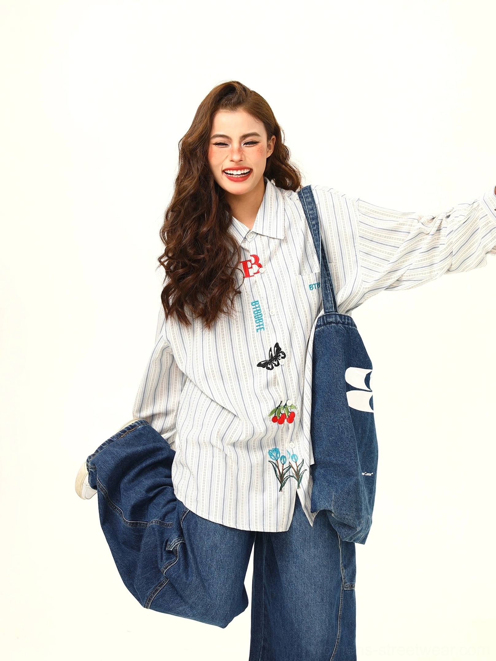 Side three-quarter view of an oversized striped shirt with front embroidery classic collar and loose sleeves paired with wide-leg denim