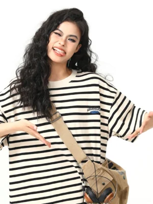 Front close-up of an oversized striped women’s streetwear T-shirt with drop shoulders, subtle chest lettering, and a canvas crossbody bag