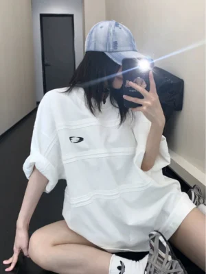 White oversized track panel jersey tee with embroidered oval logo styled as a long streetwear top with rolled sleeves