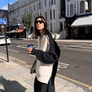 Three quarter view of relaxed oversized V-neck racing stripe sweater styled with a takeaway coffee on an urban sidewalk