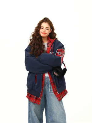 Front view of an oversized navy blue varsity patchwork layered bomber jacket with red plaid hood lining, chest embroidery, and casual blue jeans styling