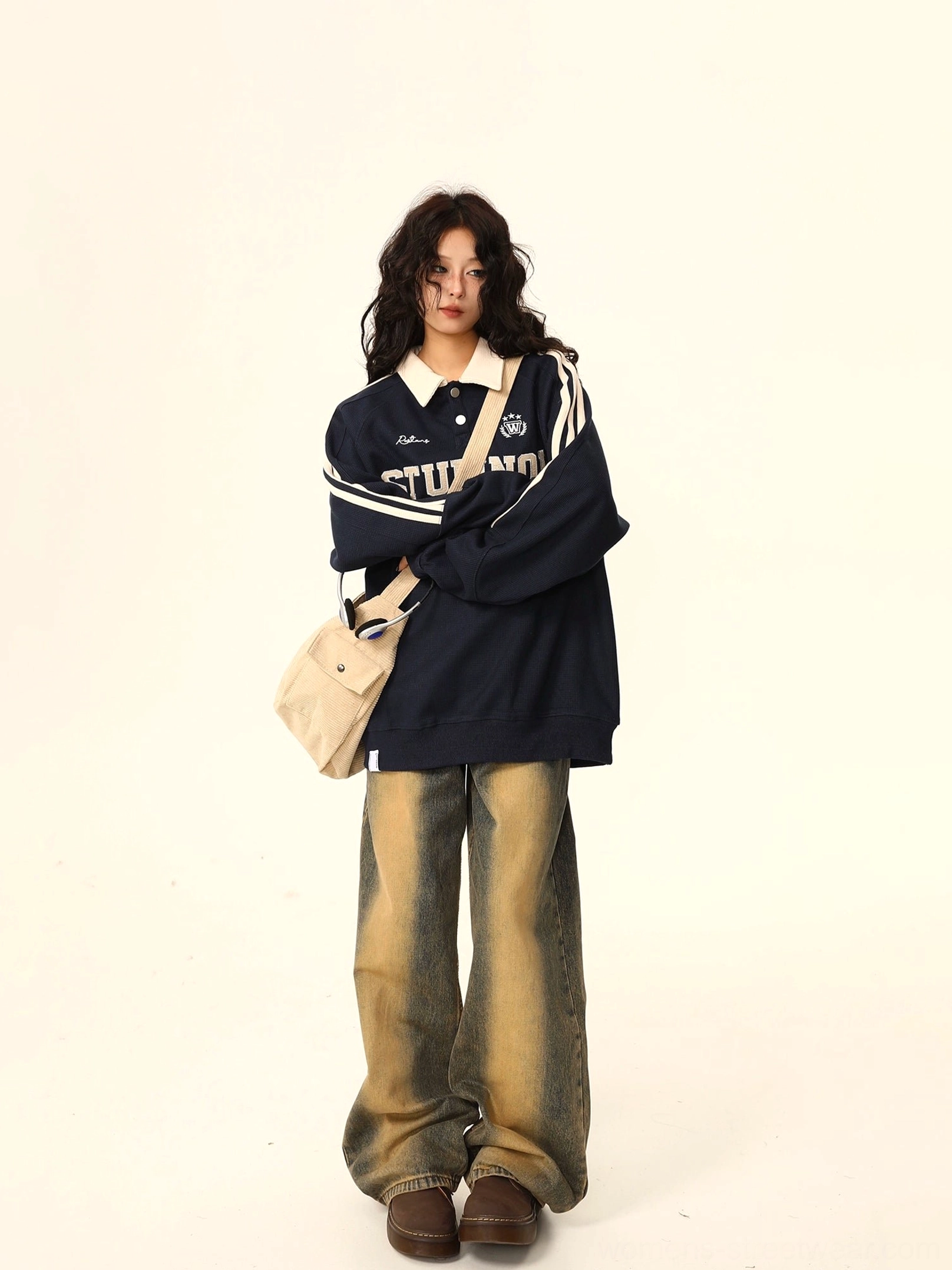 Navy blue oversized varsity polo sweatshirt with white contrast collar, athletic sleeve stripes, and embroidered collegiate lettering styled with faded wide-leg jeans