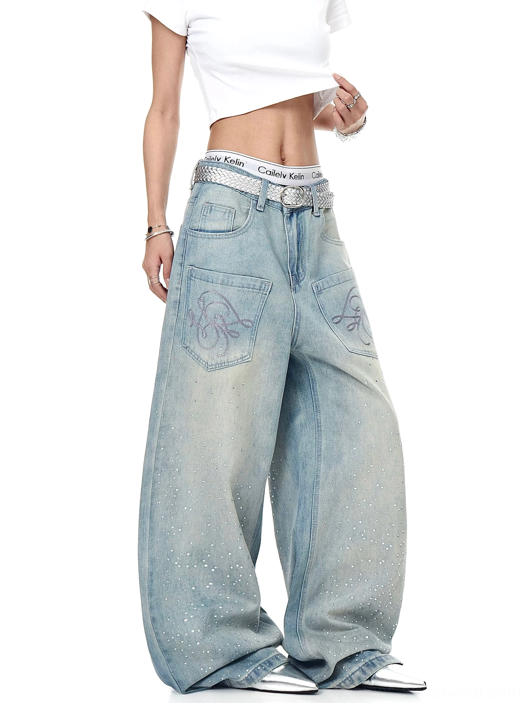 Three-quarter side view of oversized vintage blue wide-leg jeans featuring embroidered front pockets, scattered crystal studs, silver jewelry, and a relaxed streetwear fit