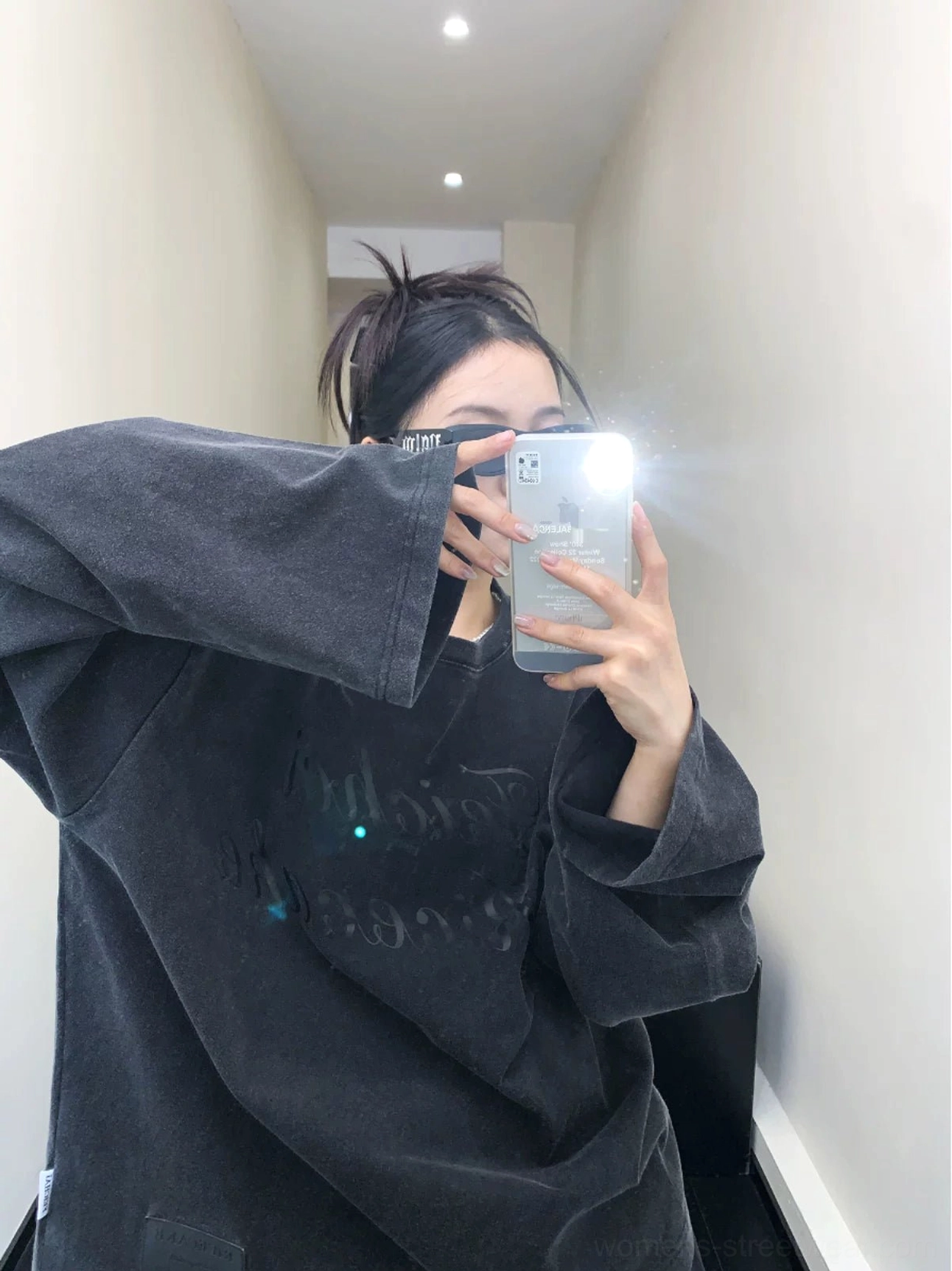 Side mirror view of an oversized washed black fleece sweatshirt with relaxed silhouette, long sleeves, and subtle front script graphic