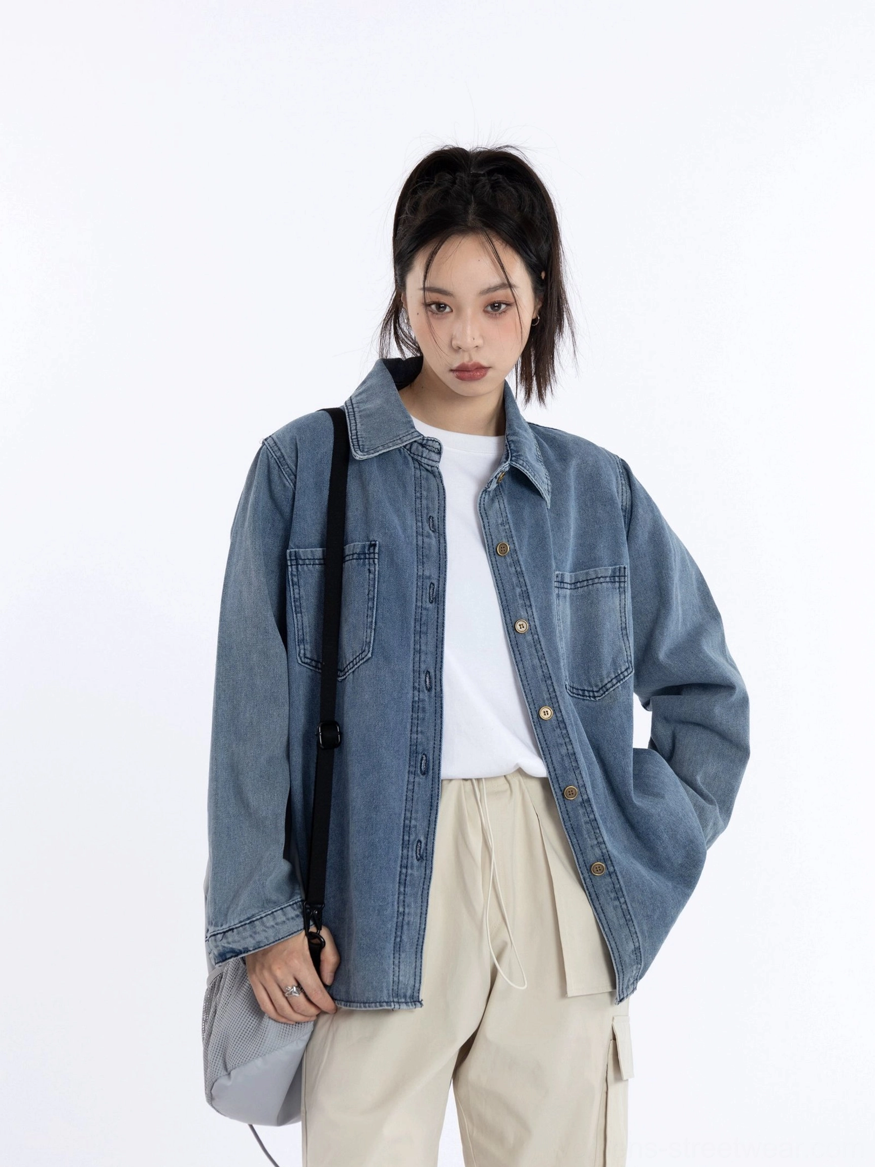 Oversized washed blue denim shirt jacket for women layered over a white tee with beige wide-leg trousers and a grey crossbody bag