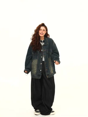 Full body front view of an oversized dark blue washed denim jacket styled with black wide leg pants and casual sneakers in a modern streetwear outfit