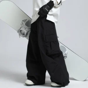 Black oversized cargo snow pants with wide-leg streetwear fit, flap thigh pockets, ski gloves, and snowboard studio styling