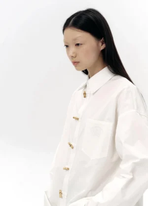 Close-up side view of white oversized cotton shirt showing pointed collar chest pocket embroidery and decorative bamboo-inspired buttons