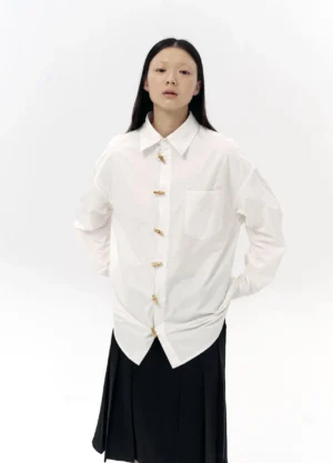 Full front view of oversized white cotton button-up shirt with bamboo-inspired buttons styled with a black pleated midi skirt
