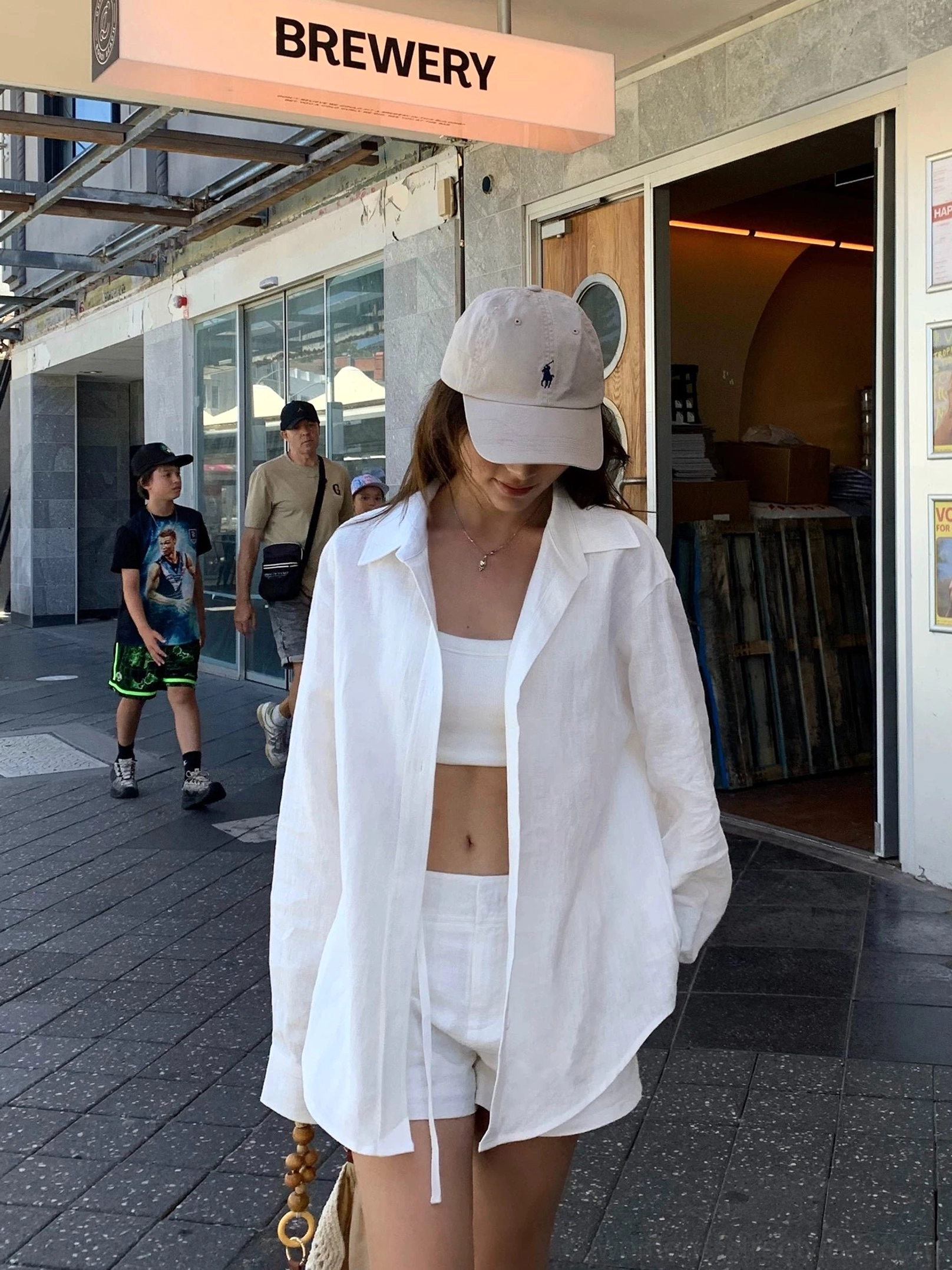 Oversized white ramie linen shirt worn open over tank top, front full-body street style shot with vintage brewery street scene background