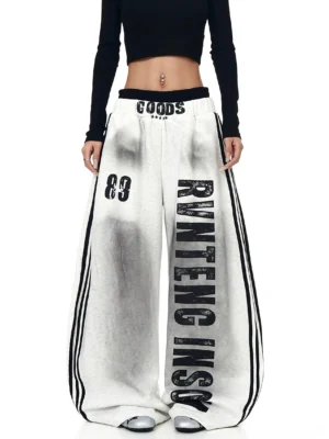 Heather gray oversized wide-leg graphic fleece sweatpants styled with a black cropped top, vertical varsity lettering, 89 graphic, and striped streetwear details