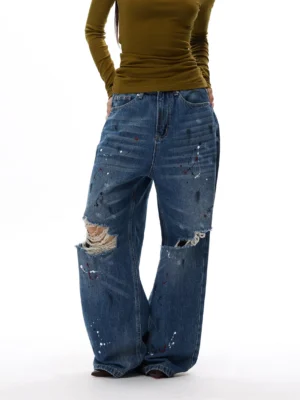 Paint splatter distressed wide-leg jeans shown from a low three-quarter front angle with frayed knees and vintage blue denim wash