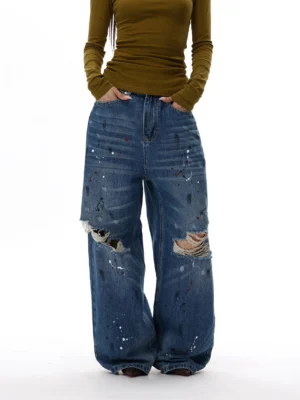 Front view of oversized paint splatter wide-leg jeans with ripped knees, faded whiskering, and relaxed streetwear fit