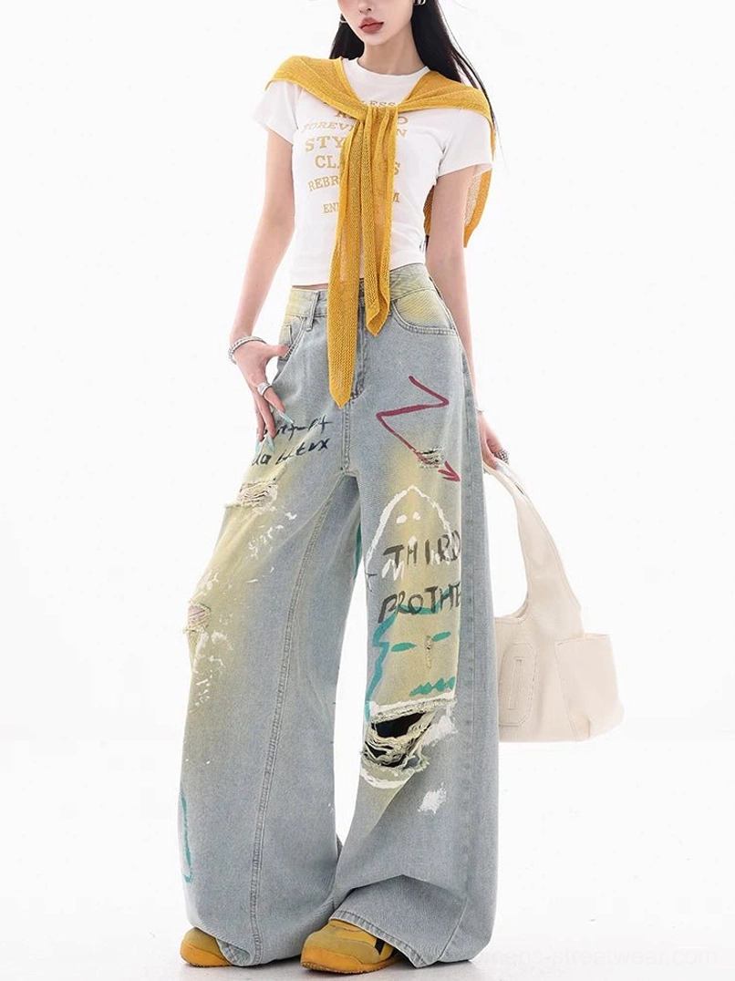 Side front view of graffiti painted patch jeans featuring colorful artwork, knee distressing, light blue acid-wash denim, and a relaxed full-length wide-leg silhouette