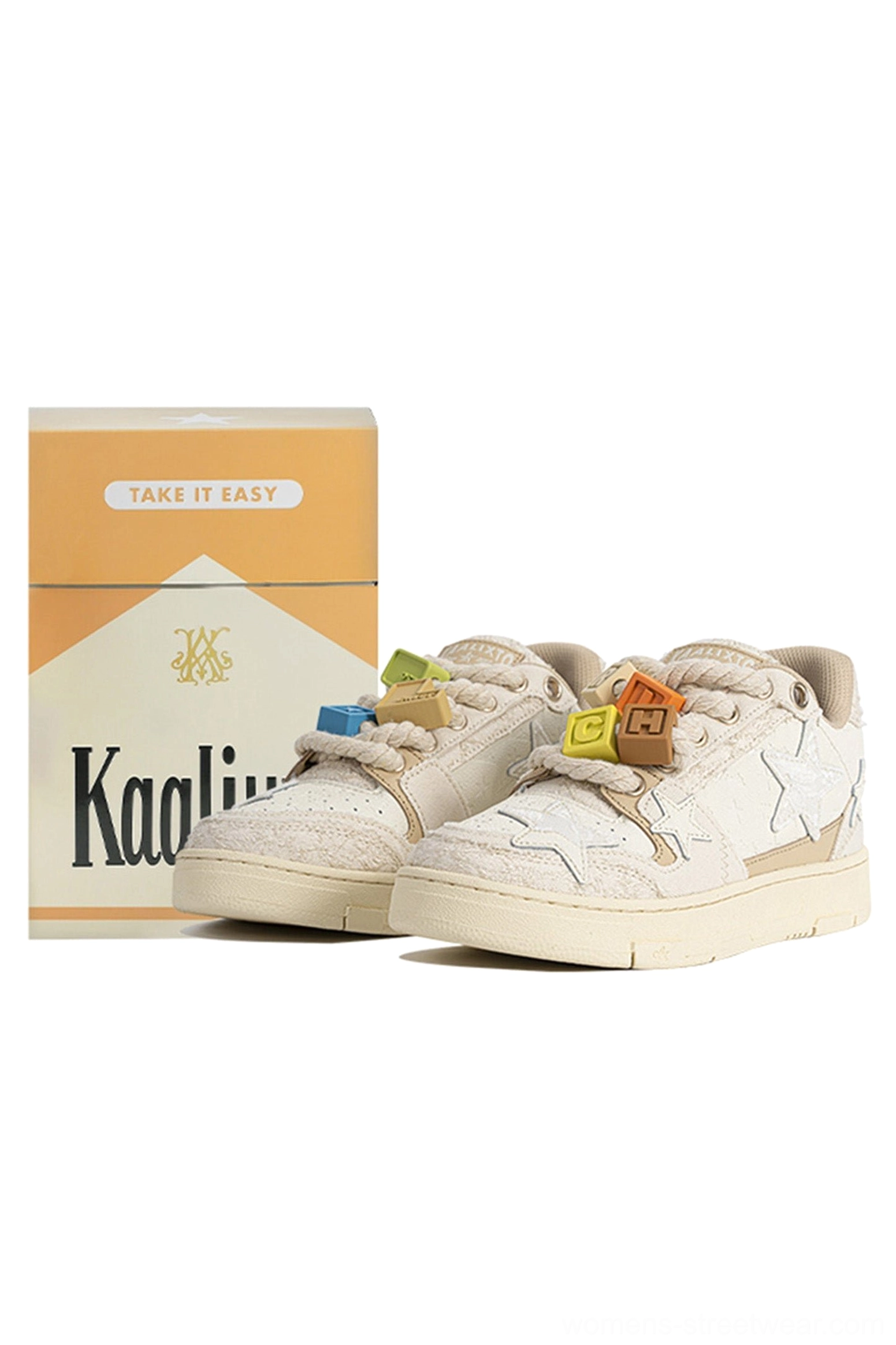 Pair of beige star streetwear sneakers shown from the front side with contrasting decorative lace charms, textured fabric upper, and casual low-top shape