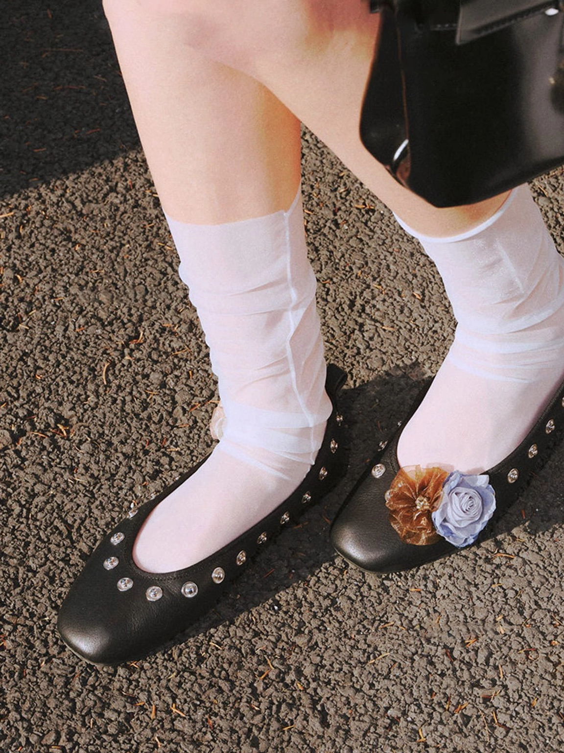 Pair of black floral square-toe flats with studded details worn with sheer ankle socks