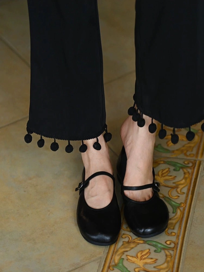 Pair of black leather Mary Jane flats worn with cropped black pants showing rounded toes and secure ankle straps