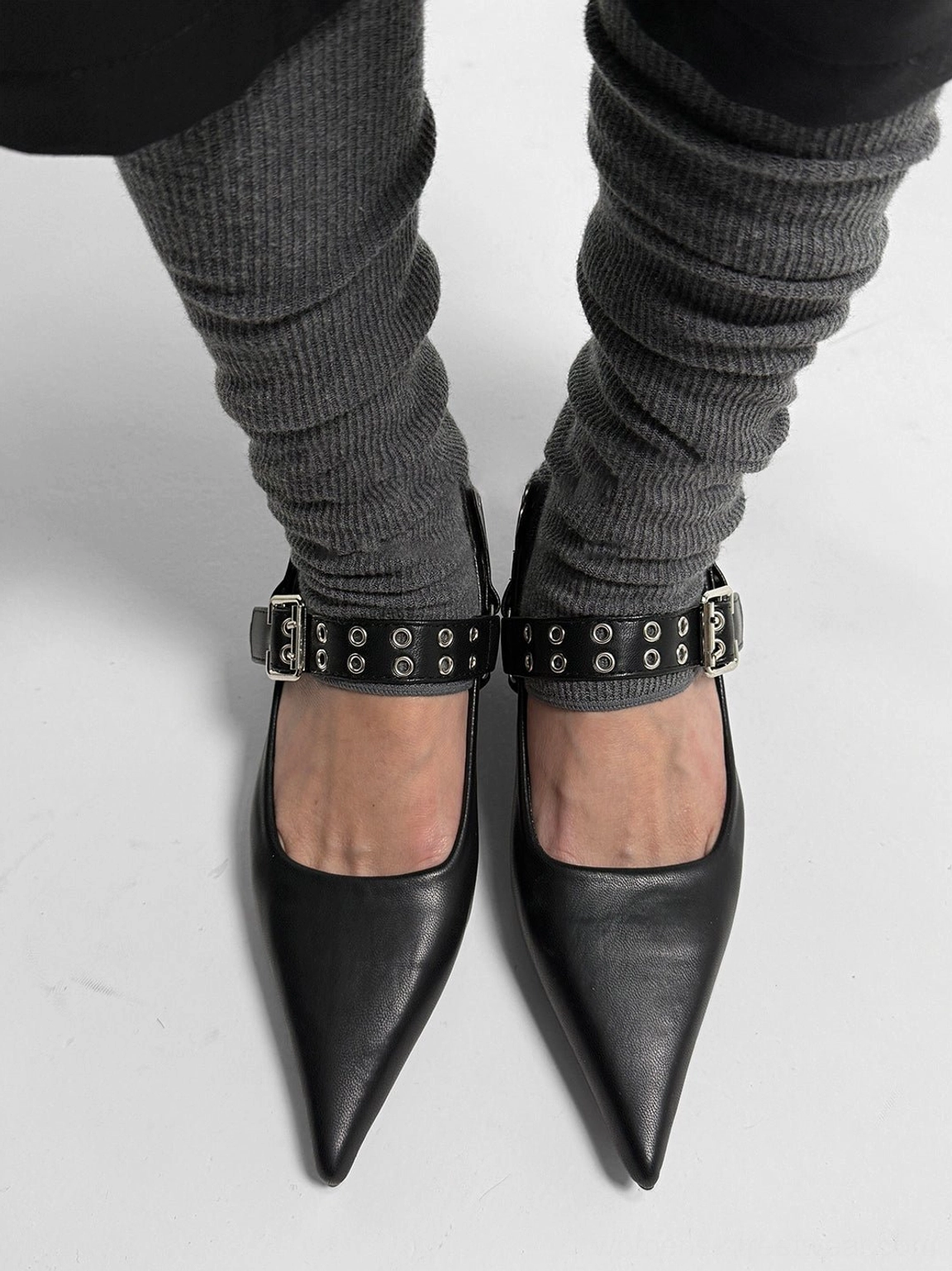 Pair of black pointed Mary Jane pumps viewed from above with matching grommet buckle straps and smooth matte finish