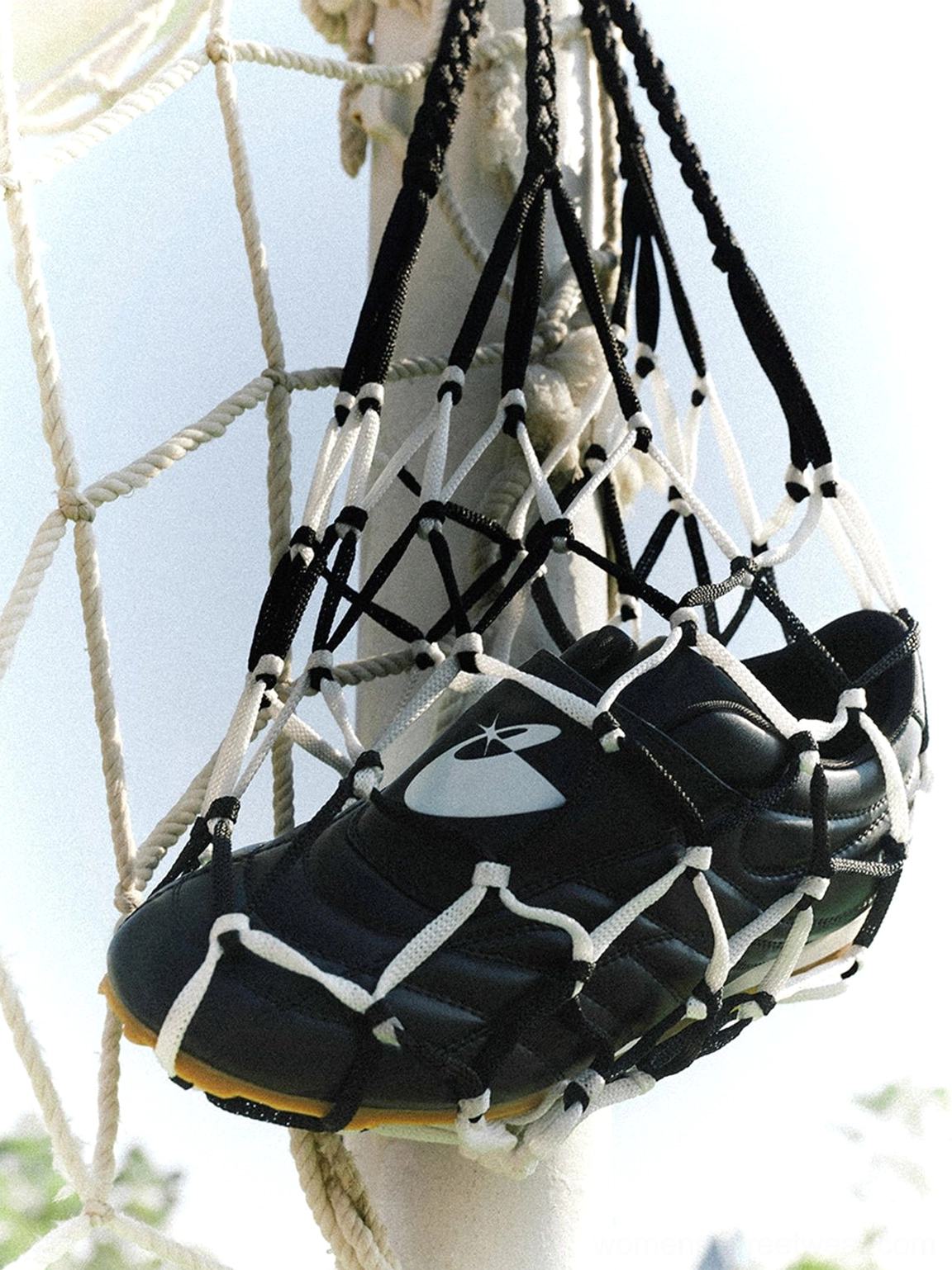 Pair of black quilted leather soccer trainer sneakers stored in a football goal net with matching gum rubber soles