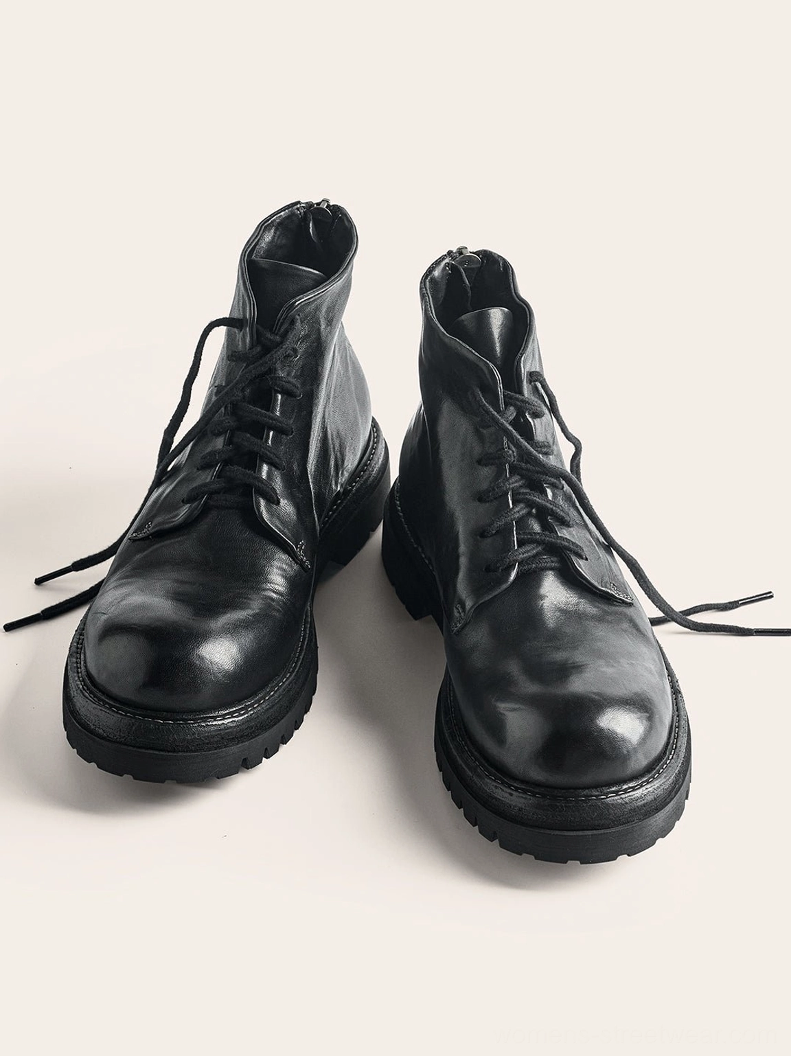 Pair of black washed horsehide combat boots shown from the front with round toes, neat laces, textured leather uppers, and heavy lug soles