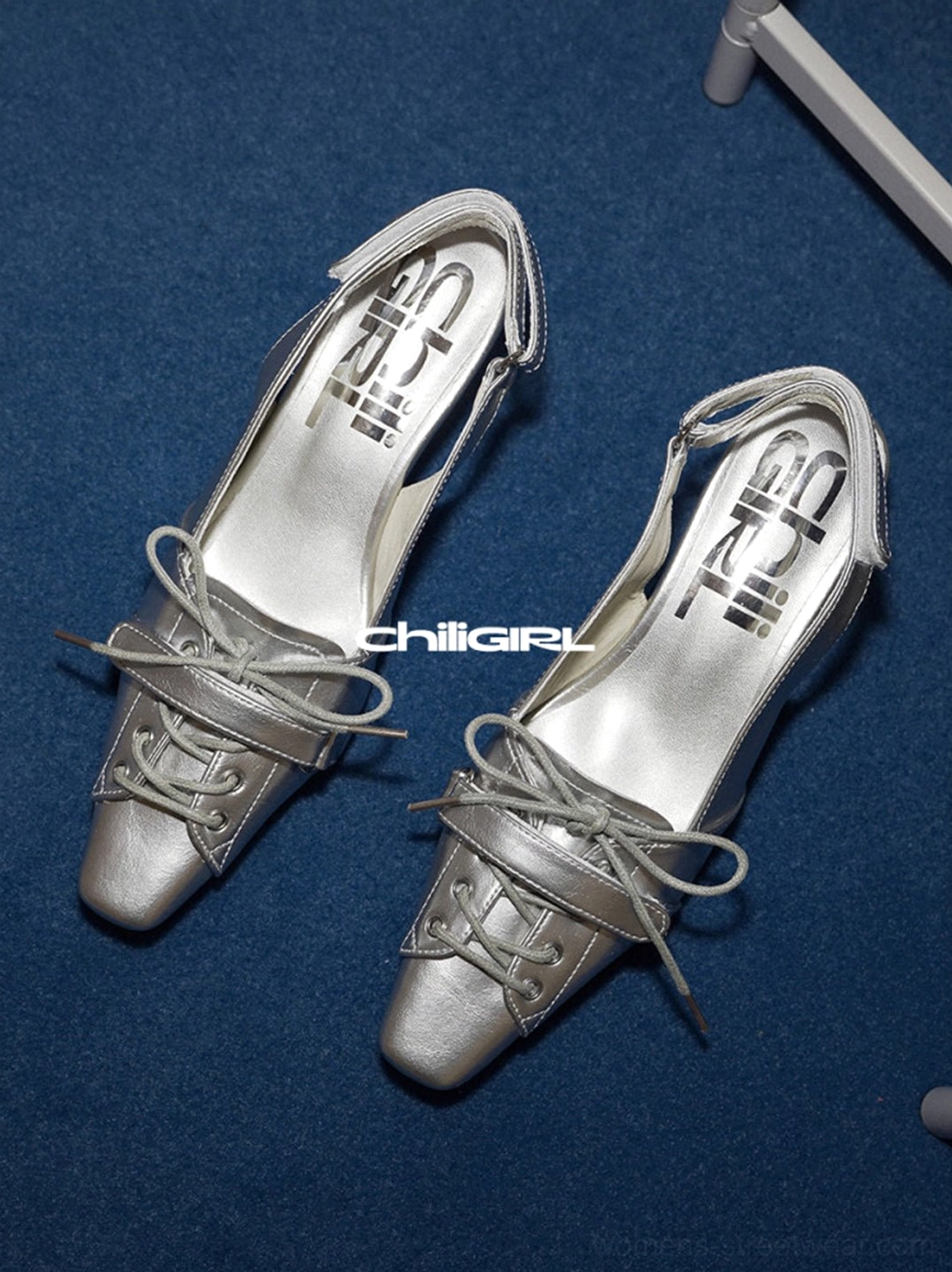 Pair of silver pointed-toe kitten heel slingback shoes with bow detail shown on a dark blue background