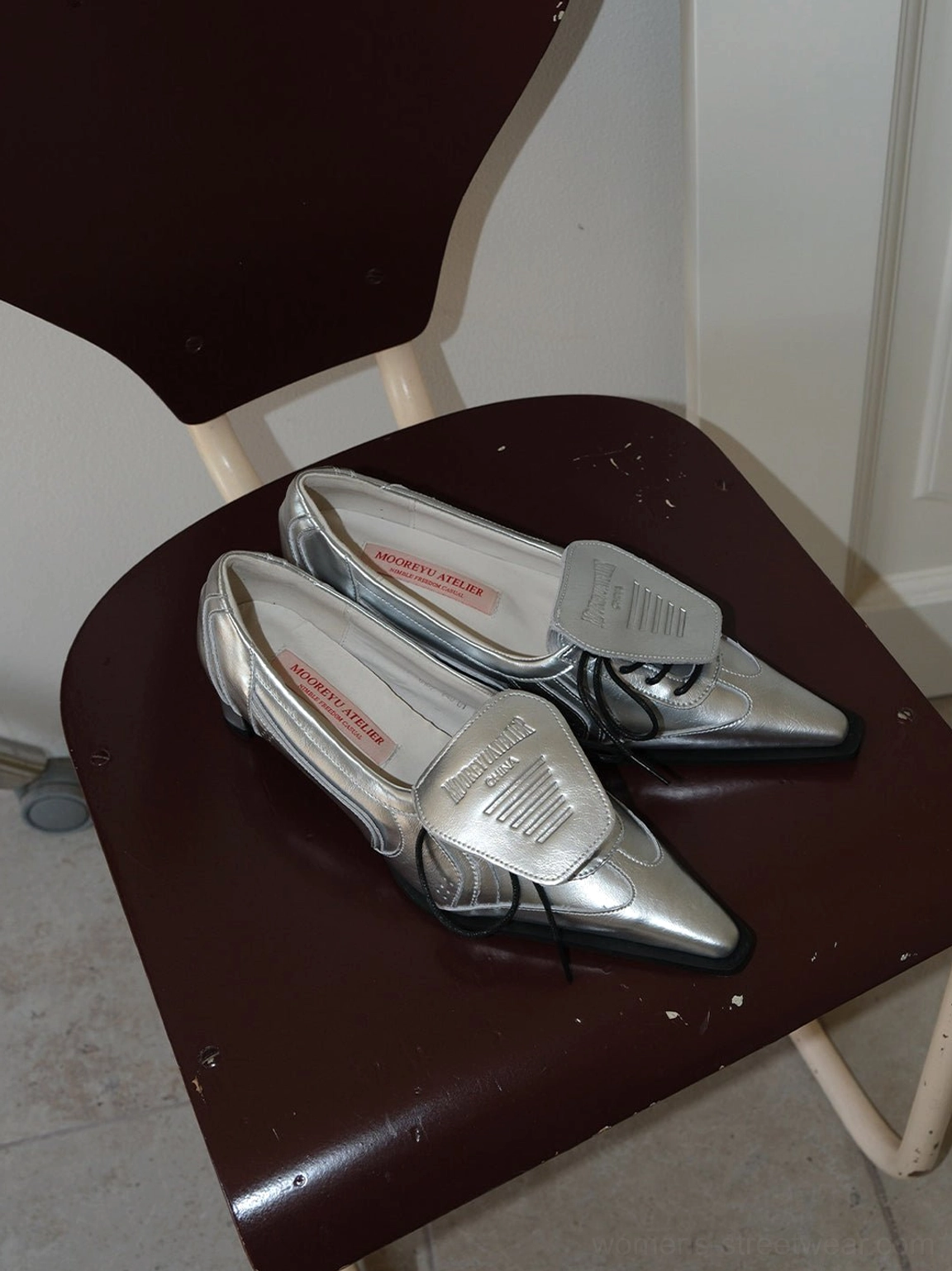 Pair of silver pointed-toe leather-look pumps with removable lace flap displayed on a dark brown chair