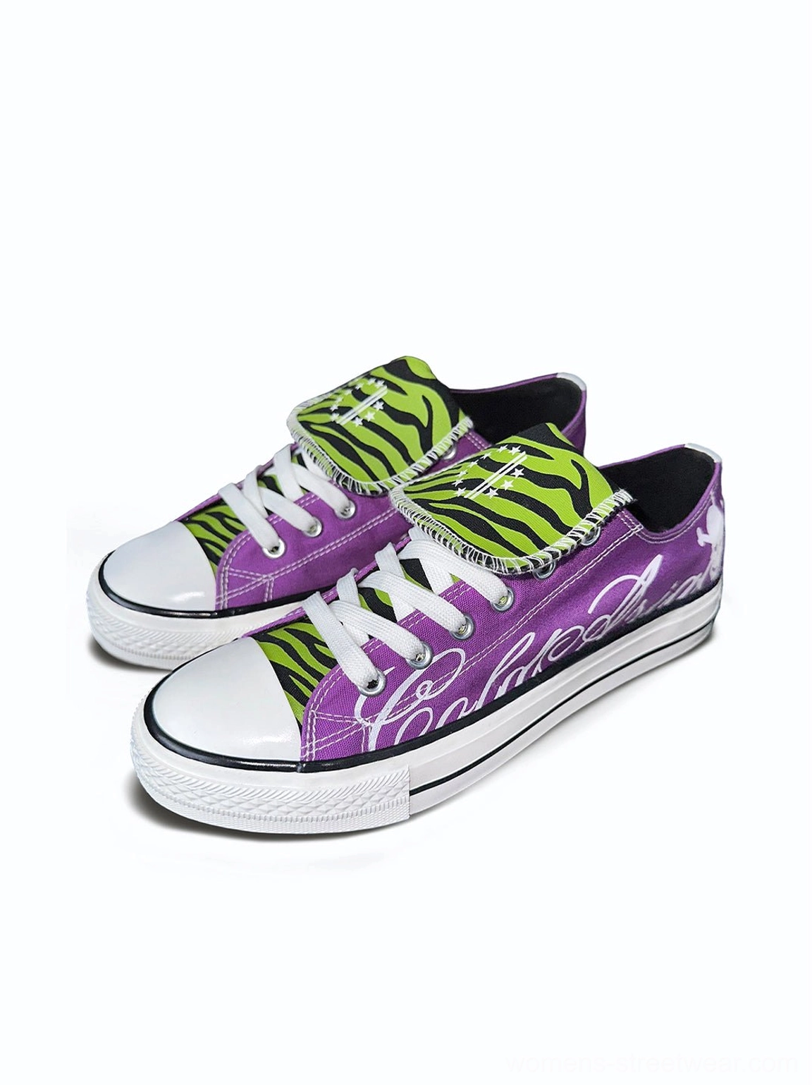 Pair of purple low top graphic canvas sneakers with white cursive lettering, exposed green zebra tongues, white rubber soles, and skull heel logos
