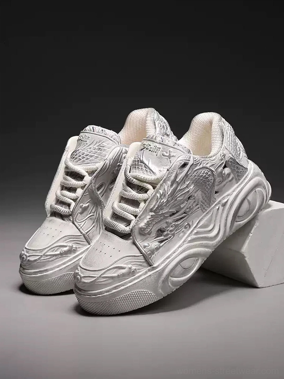 Pair of white dragon relief platform sneakers displayed from the front three-quarter angle with chunky sculpted soles