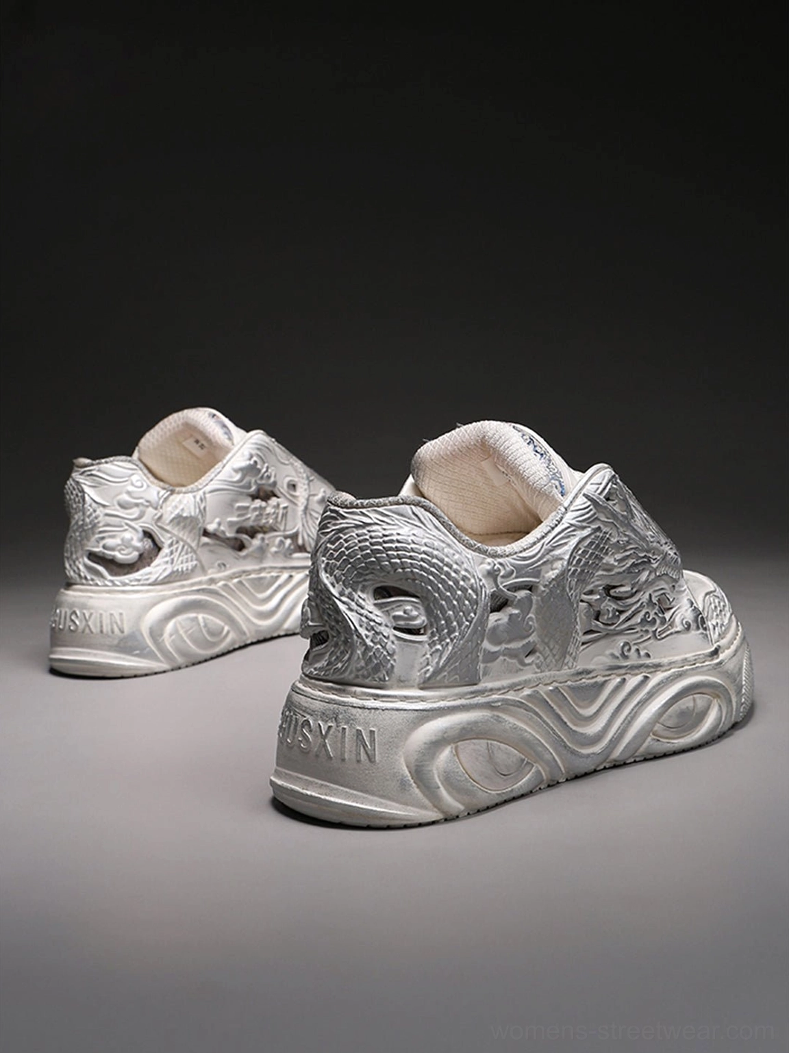 Pair of white dragon relief sneakers shown from the rear three-quarter angle with sculpted chunky platform soles