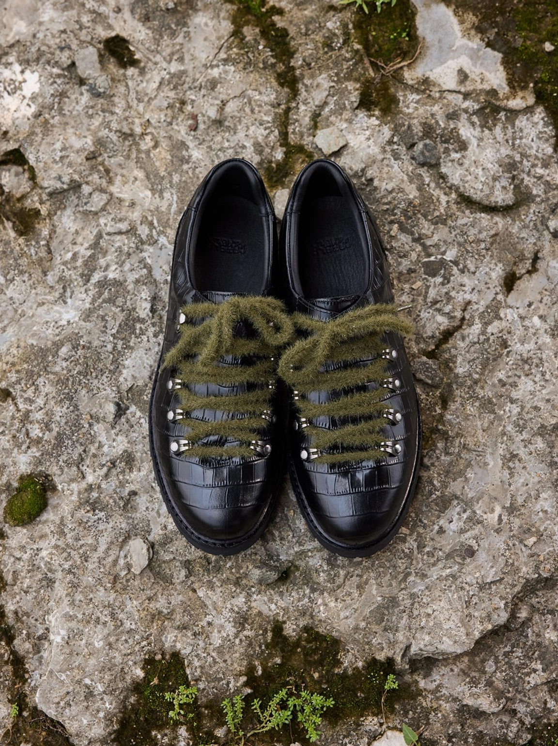 Paired black genuine leather derby shoes with glossy crocodile embossing, silver lace eyelets, and olive green laces