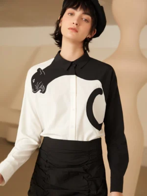 Front view of black and white panther embroidered color block blouse styled with a black beret and ruched midi skirt